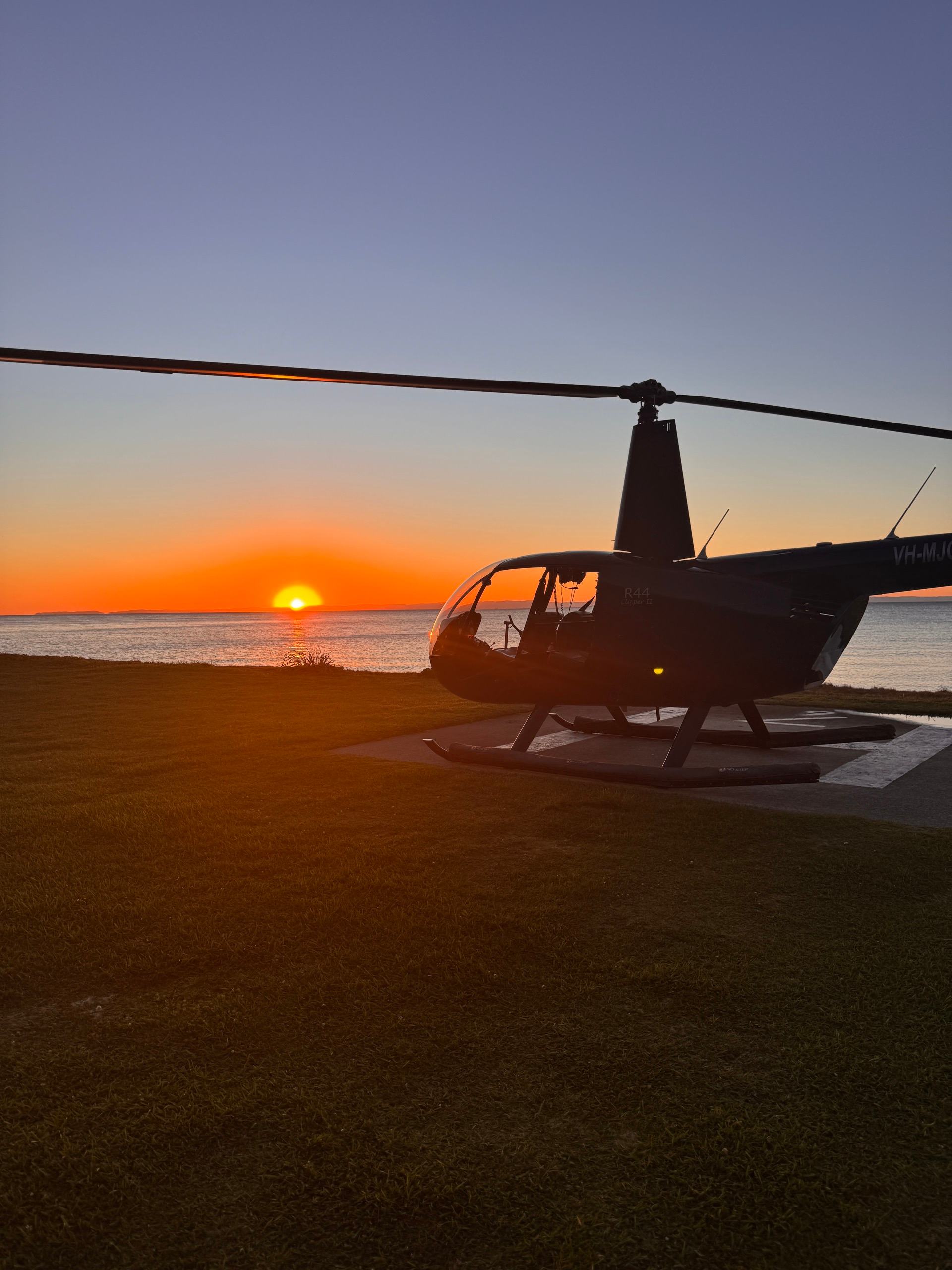 A Vantage R44 on the grass at sunset, the sun going down over the water behind it